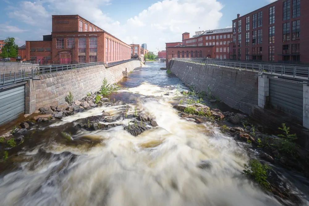 Tammerkosken virta punatiilisten tehdasrakennusten välissä, kivetyt rantamuurit ja kaiteet molemmin puolin